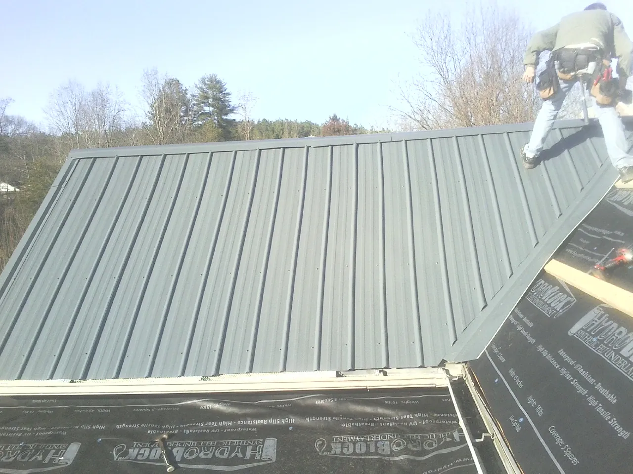 Crew installing dark green standing seam panels over synthetic underlayment in Petaluma