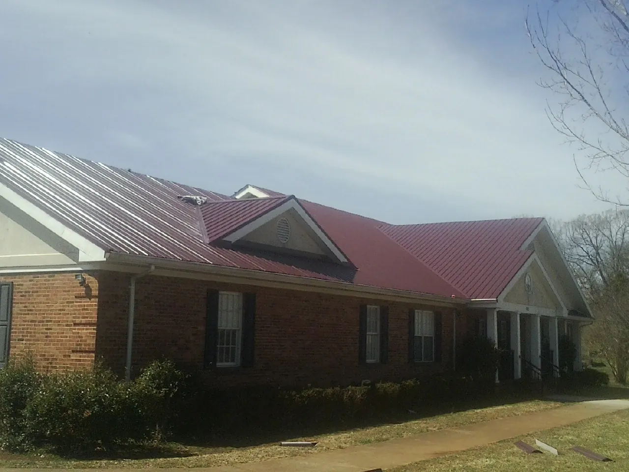 Red metal roof with gabled entries on a long brick building, from a Hail Damage Roof Repair job in Petaluma